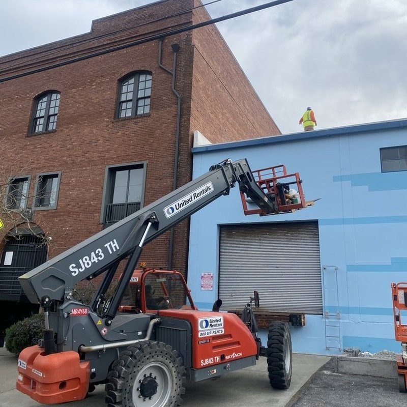 Telehandler beside a brick and blue industrial building in San Francisco