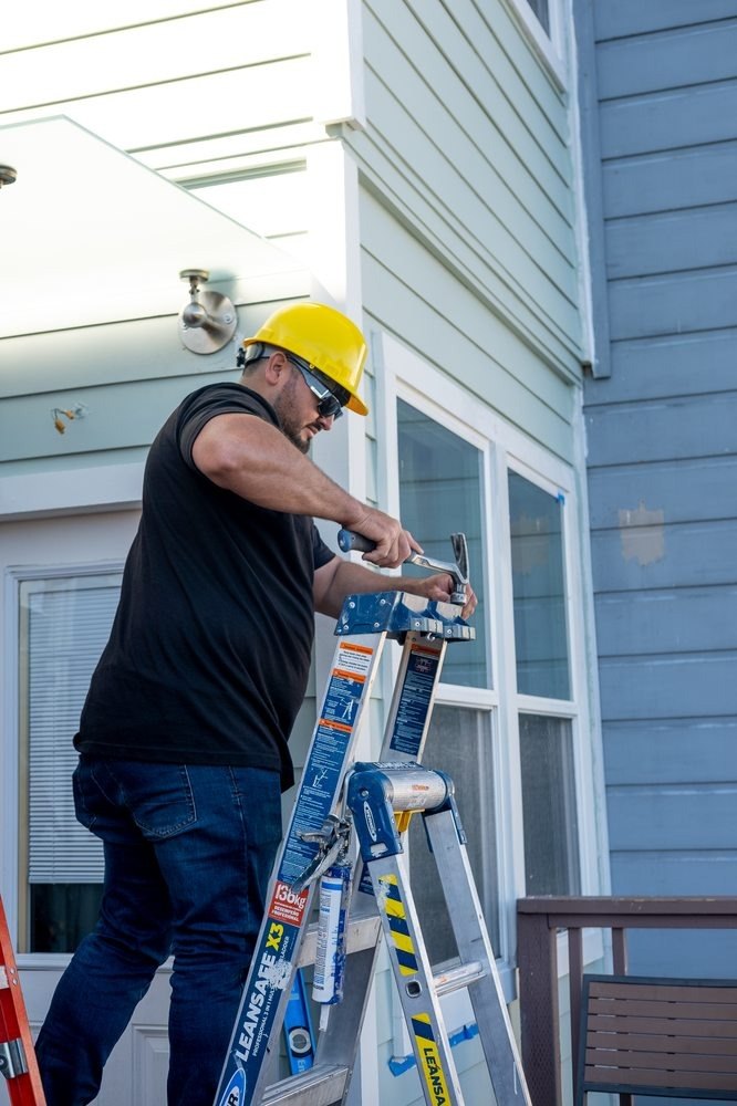 Contractor in a hard hat working from a ladder at a window